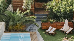 A pool area with wooden deck, lounge chairs, and a variety of tropical plants.