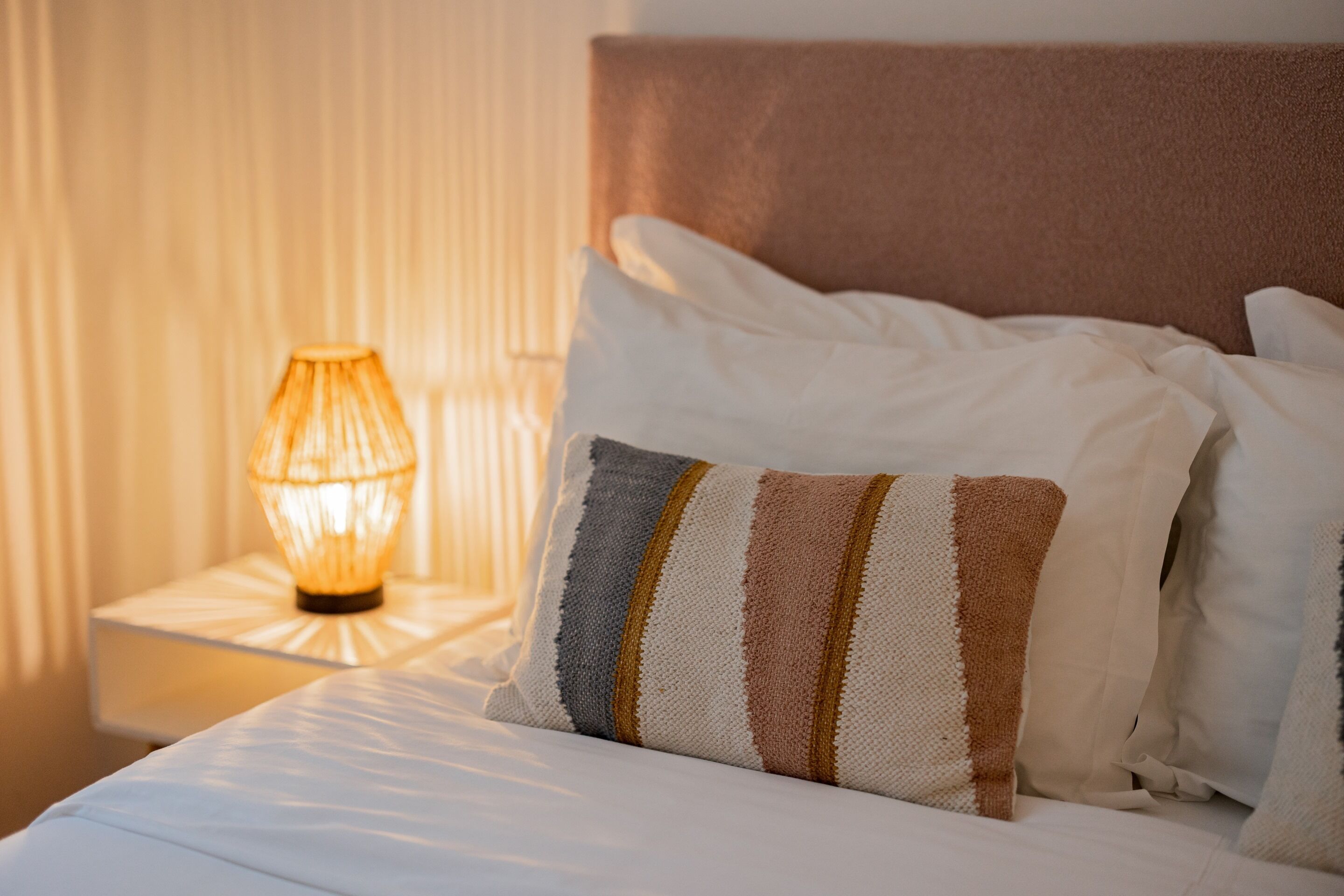 A neatly made bed with striped pillows and a bedside lamp.