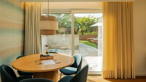 A room with a round table, chairs, a hanging light fixture, and a view of a garden through a glass door.