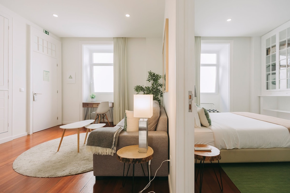 A modern hotel room with a bed, a sofa, a desk, and a lamp.