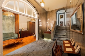 A spacious lobby with a wooden reception desk, a staircase, and a large mirror. - Casa do Contador - Suites & Pool (Ponta Delgada)