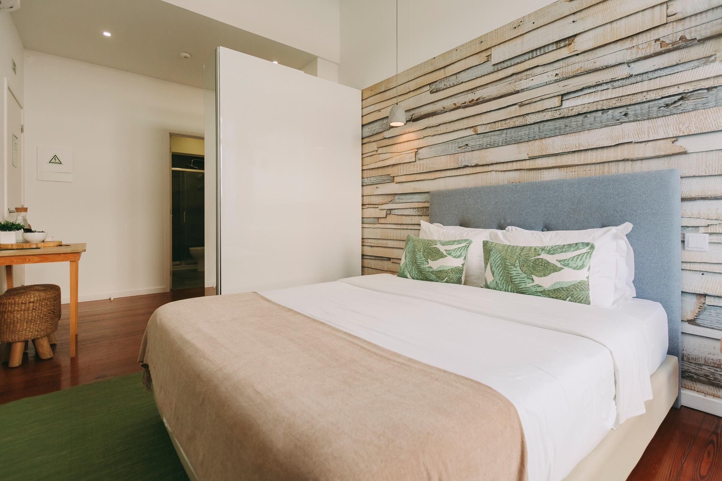 A bedroom with a large bed, a wooden headboard, a desk with a chair, and a green rug.