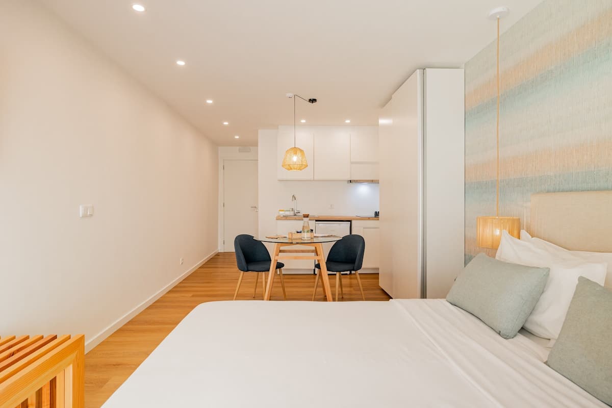Una habitación de hotel moderna con una cama grande, un escritorio con dos sillas y una cocina al fondo.