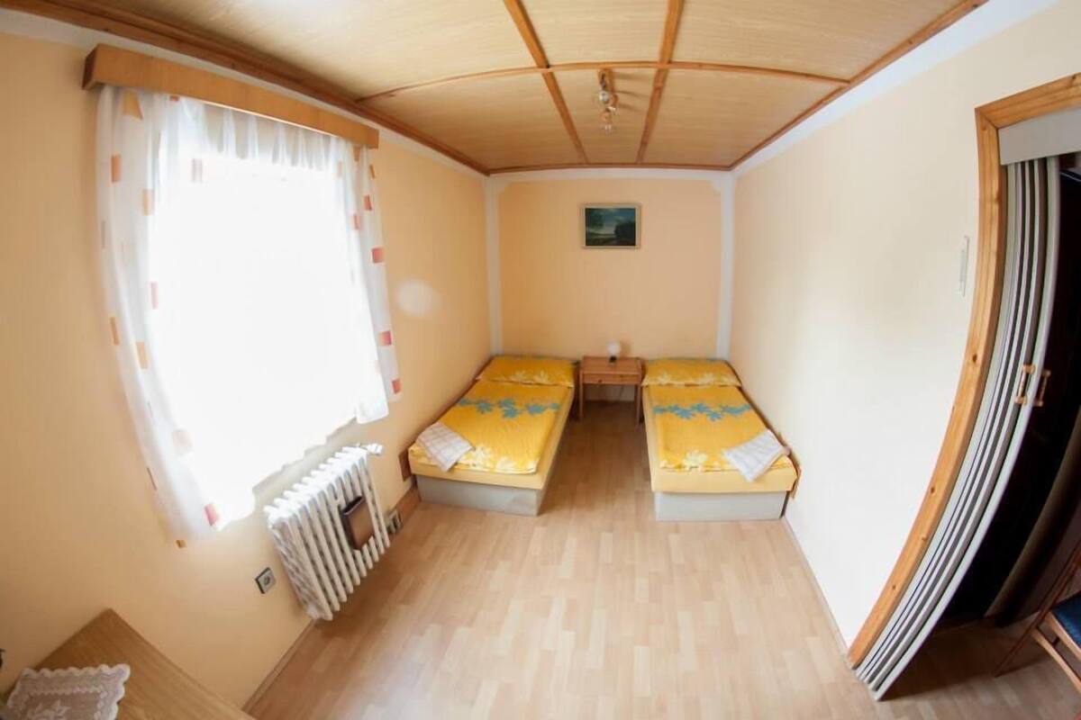 A compact room with two beds, a small table, and a window with curtains.