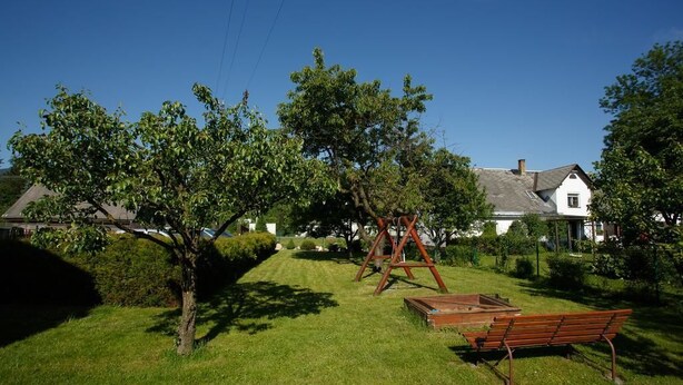 A grassy area with a wooden swing set, a bench, and a tree. - Penzion Mona (Bela pod Pradedem)