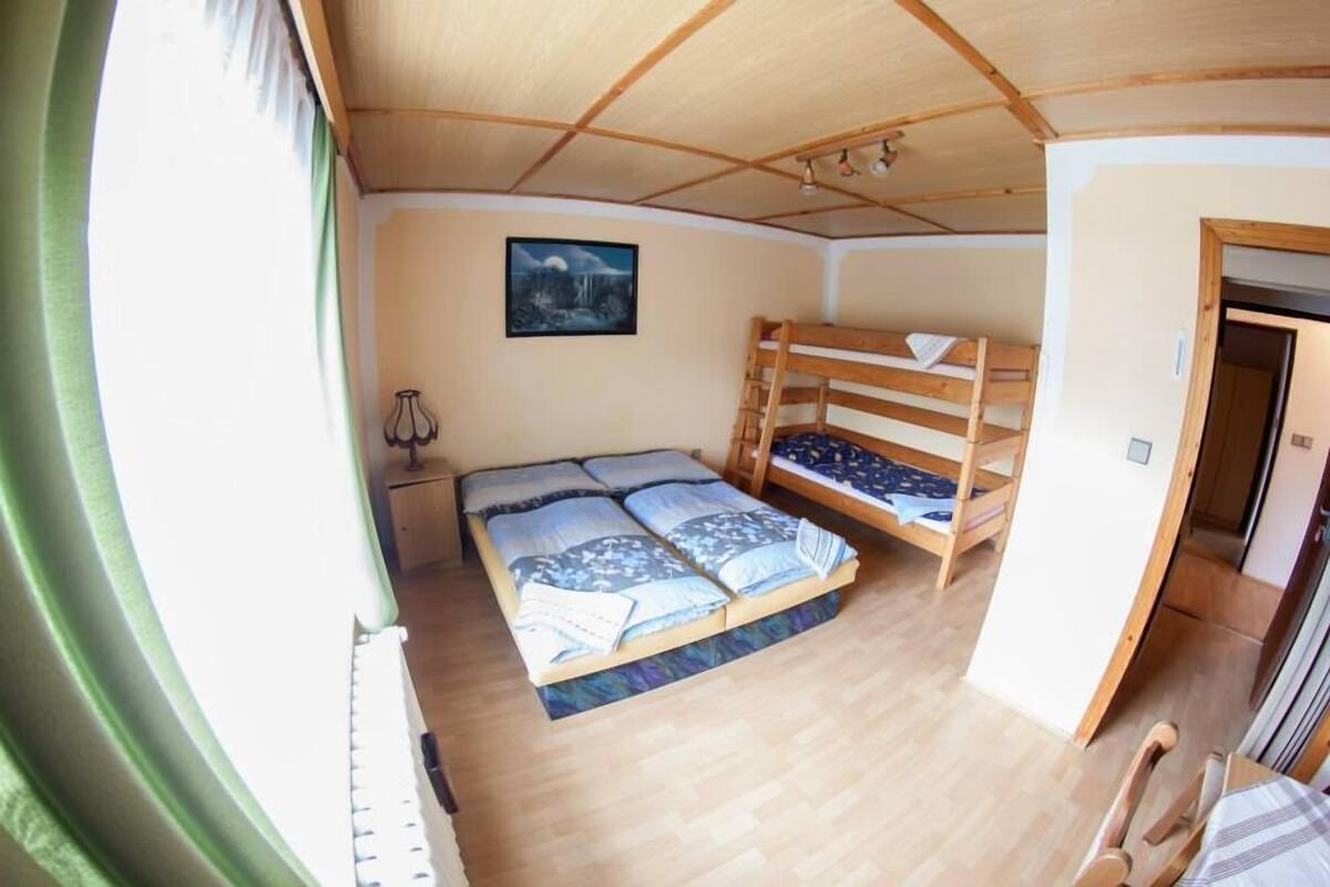 A room with a bunk bed, a desk, and a chair. There is a window with curtains, a picture on the wall, and a door.
