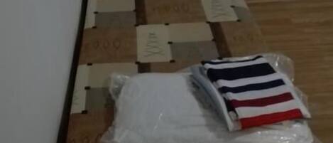 A small room with a wooden floor and a bed with a striped blanket. There are several cardboard boxes stacked against the wall.