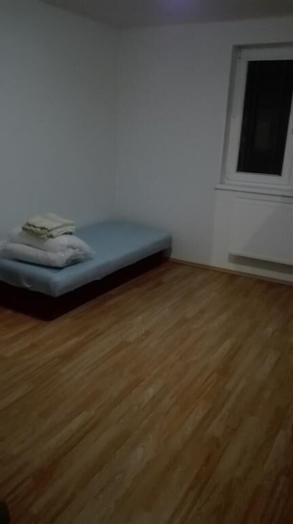 A room with a single bed, a window, and wooden flooring.