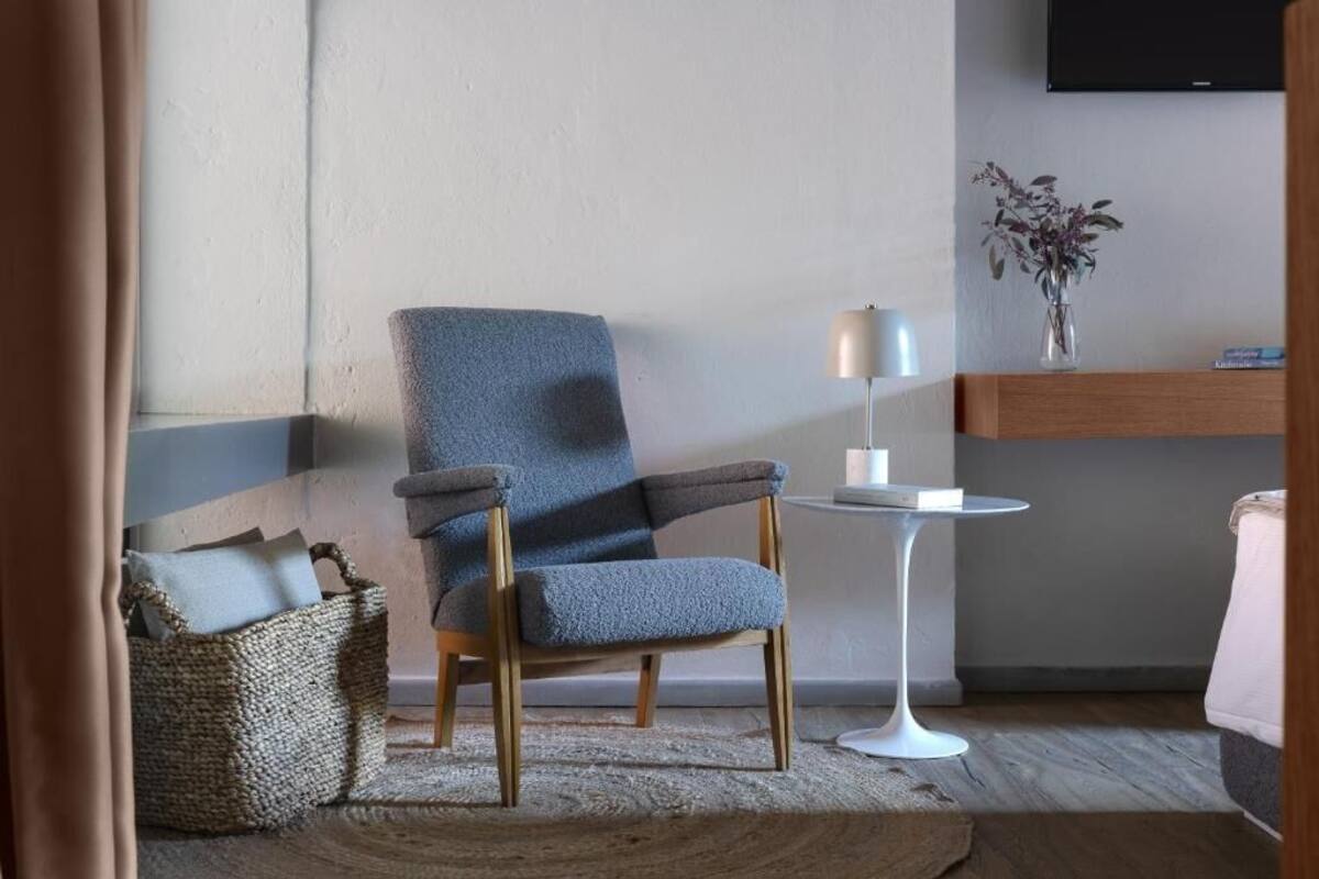 A modern room with a blue armchair, a small white table, a lamp, and a vase with dried flowers on a shelf.