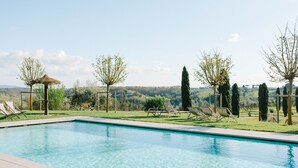 A swimming pool with clear water, surrounded by lounge chairs and trees. - Salvadonica - Borgo del Chianti (San Casciano in Val di Pesa)