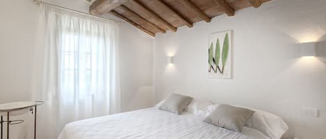 A bedroom with a bed, a bedside table, a window with curtains, and a wall-mounted light fixture.