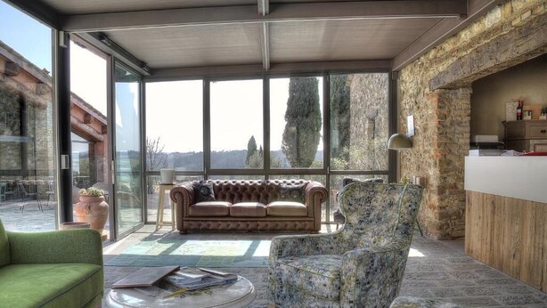 A spacious living area with a large window, a sofa, a green armchair, and a patterned armchair. - Salvadonica - Borgo del Chianti (San Casciano in Val di Pesa)