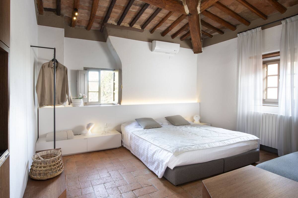 A bedroom with a bed, bedside tables, a hanging light fixture, a window, and a ceiling fan.