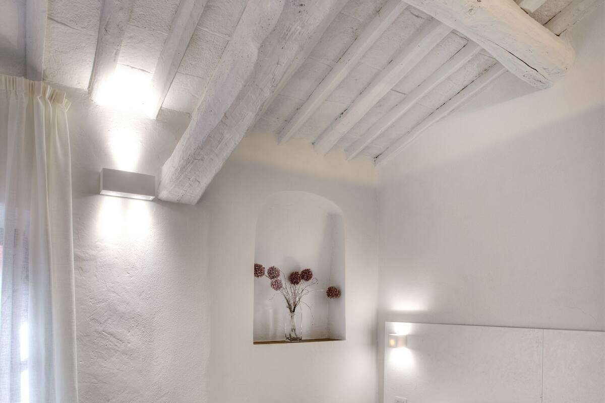 A bedroom with a large bed, a wall-mounted light, and a painting of flowers.