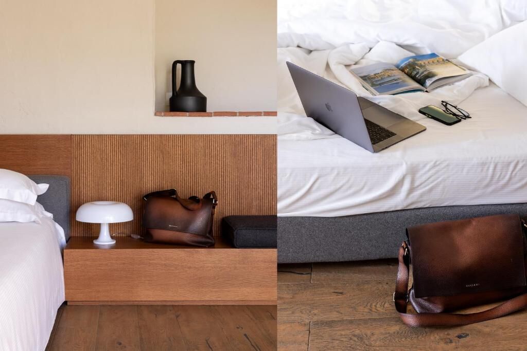 Une chambre d’hôtel avec une tête de lit en bois, une table de chevet avec une lampe et un sac à main, et un lit sur lequel se trouvent un ordinateur portable, un livre et des lunettes.