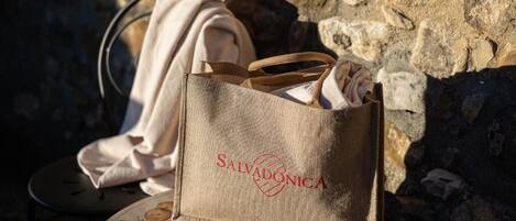 A burlap tote bag with the text "SALVADONICA" on it, placed on a table with a floral pattern.