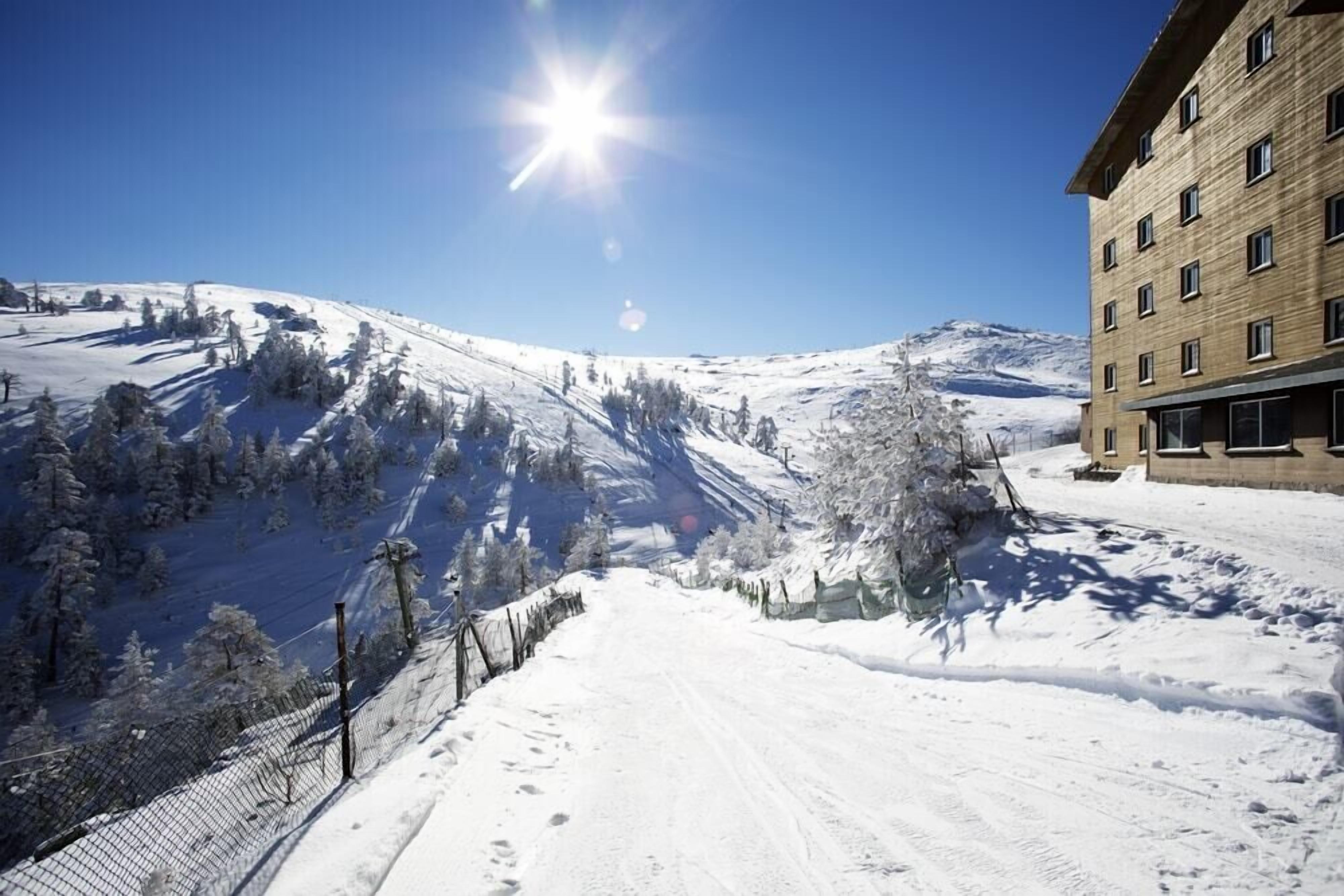 Un sendero nevado en la montaña con un edificio a la derecha.
