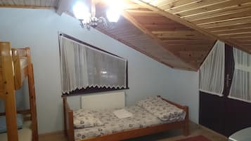 A small, cozy room with a wooden ceiling, a single bed with floral bedding, a radiator, and a window with lace curtains.