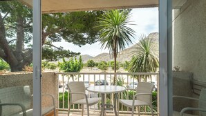 A balcony with wicker chairs and a table, overlooking a parking area and greenery. - Apartamentos Massol (Pollenca)