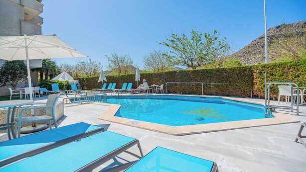 A swimming pool with lounge chairs and umbrellas, surrounded by a landscaped area with a hedge and a building in the background. - Apartamentos Massol (Pollenca)