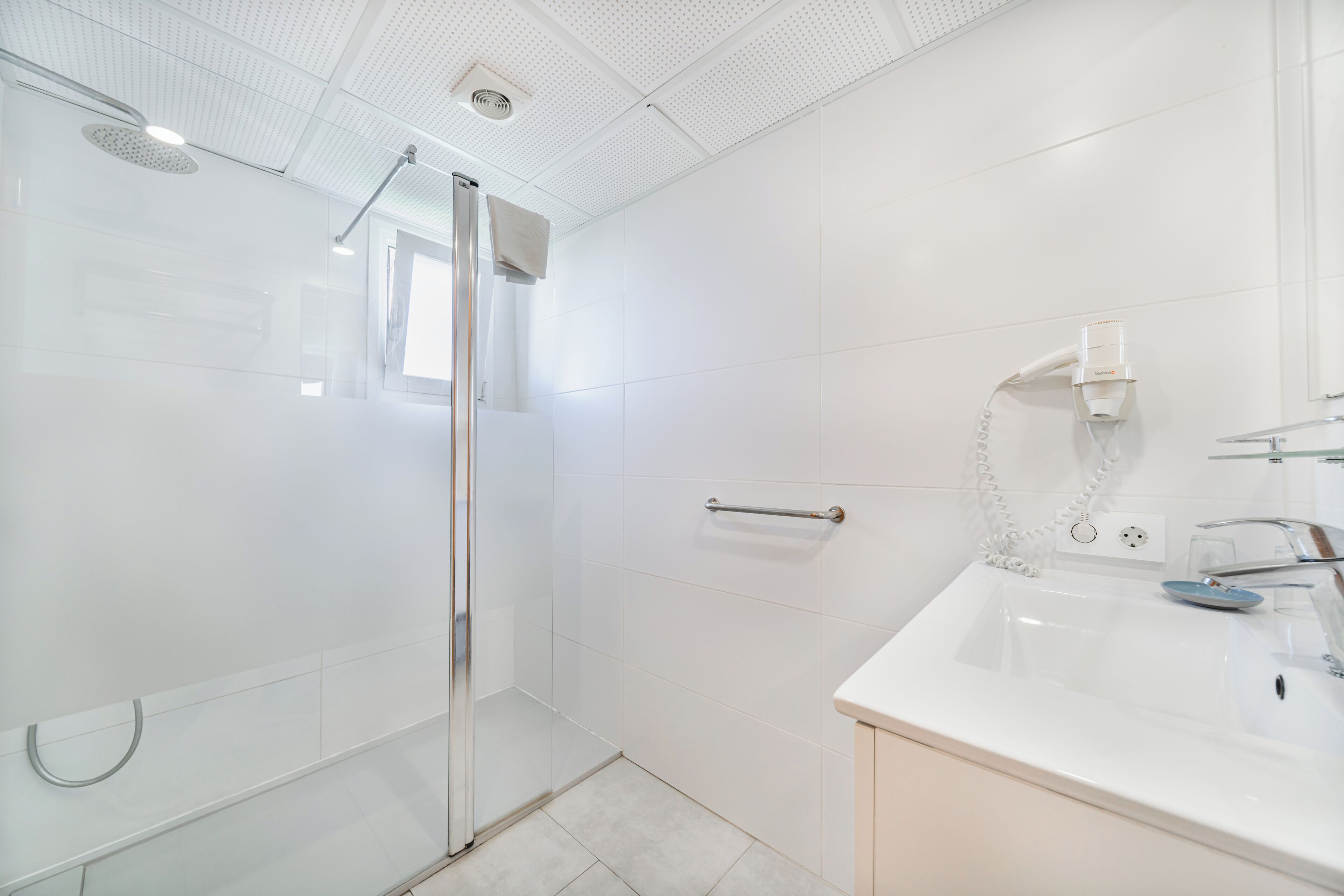 A modern bathroom with a glass shower enclosure, a white sink with a mirror, and a towel rack.
