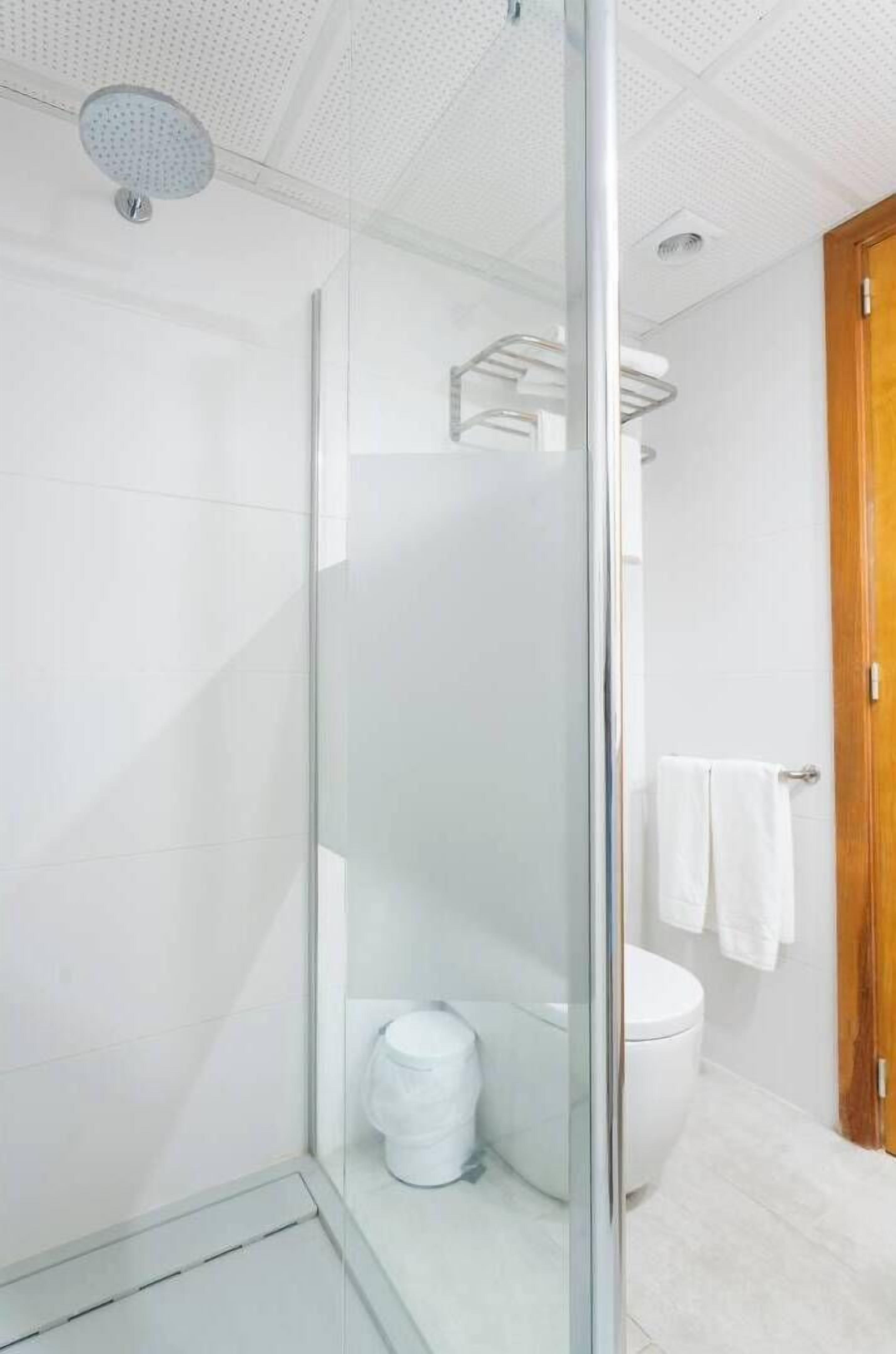 A modern bathroom with a glass shower enclosure, a toilet, and a wooden door.