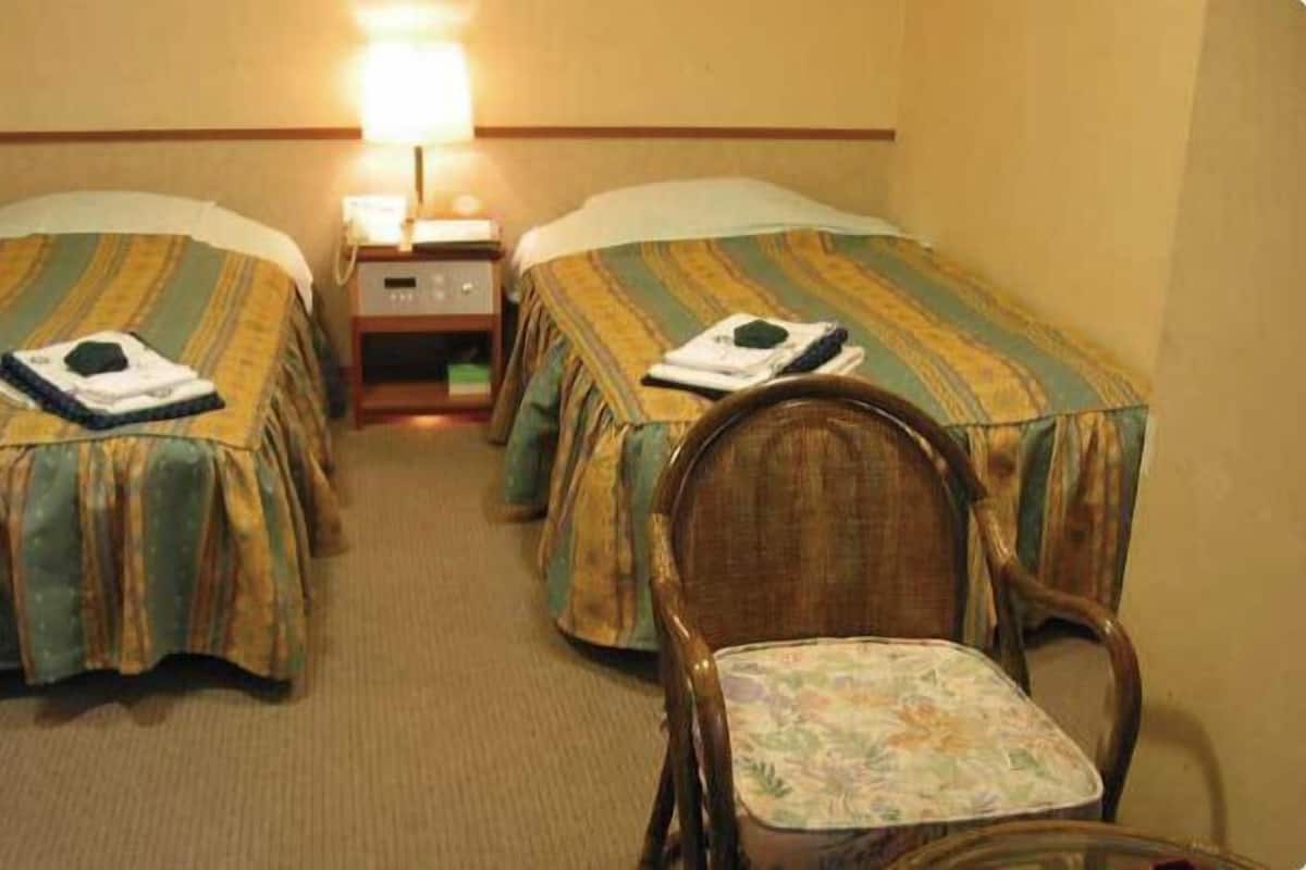 Ett hotellrum med två separata sängar, ett nattduksbord, en lampa och en stol i trä.