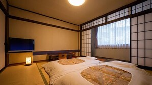 Una habitación tradicional japonesa con suelo de tatami, futón, televisor y puertas correderas shoji.
