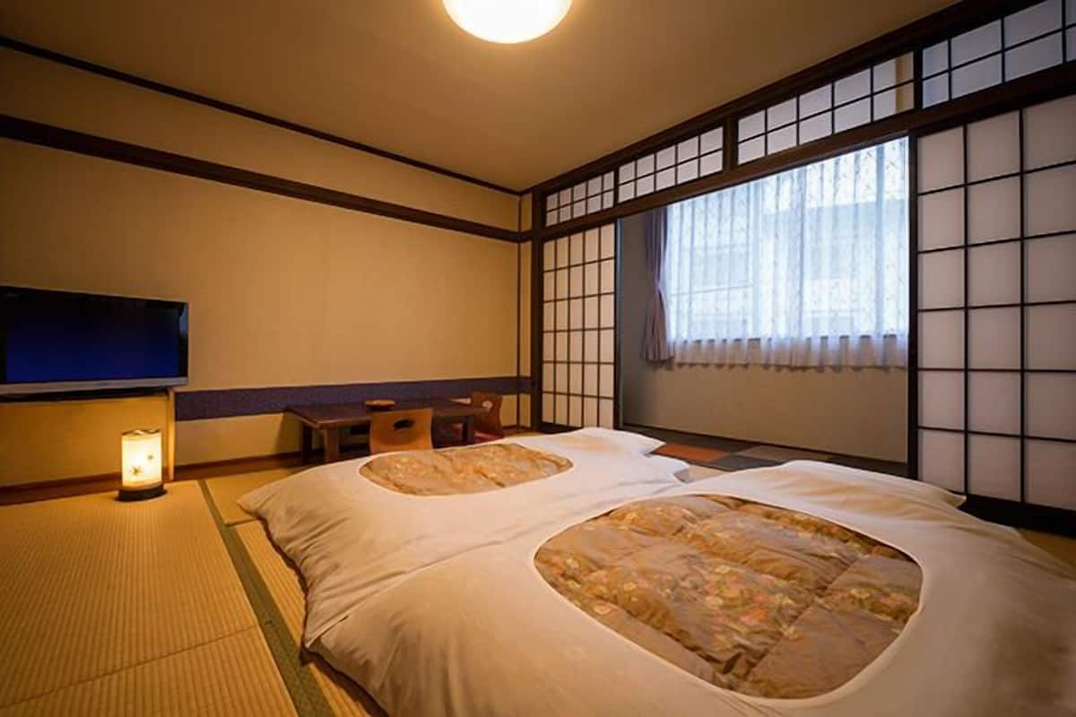 Ett traditionellt japanskt rum med tatamimattor på golvet, en futonmadrass, en tv och en skjutbar shojiskärm.