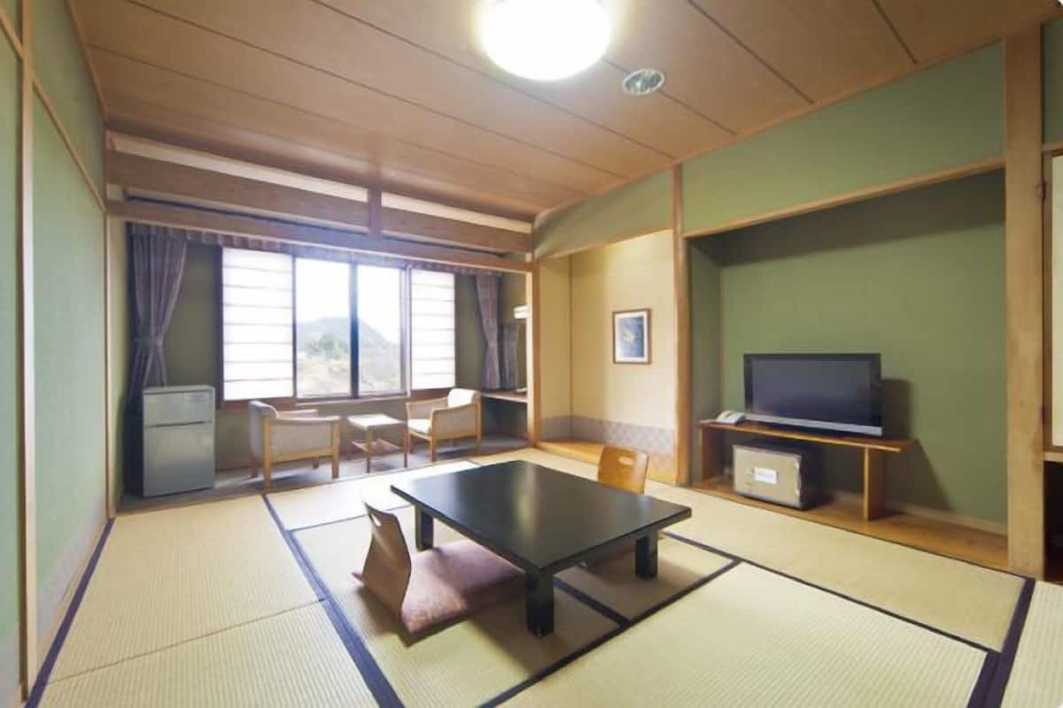 Ett traditionellt japanskt rum med tatamimattor på golvet, ett lågt bord, en tv och utsikt över naturen genom stora fönster.