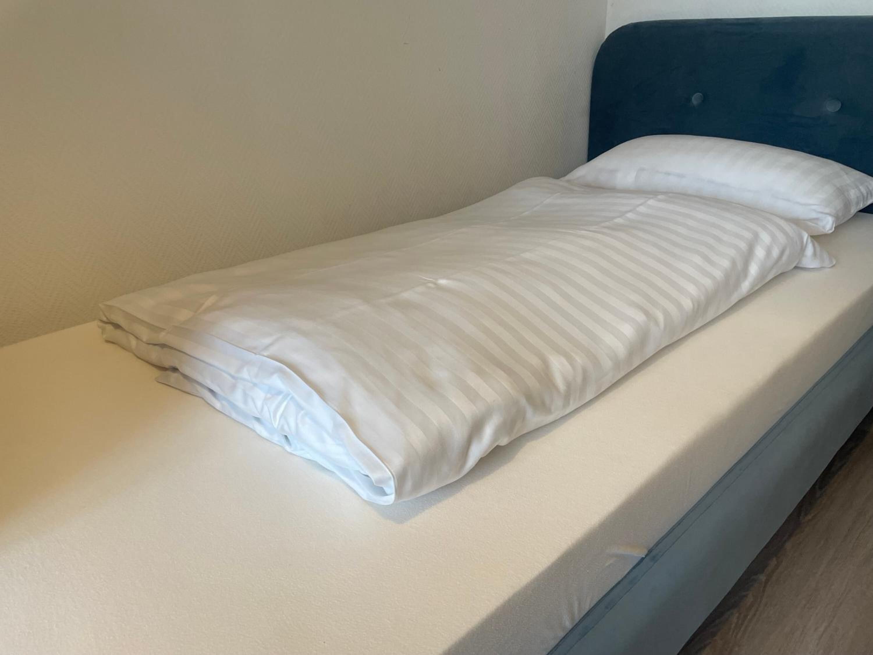 Ein Einzelbett mit weißer Matratze und blauem Kopfteil.