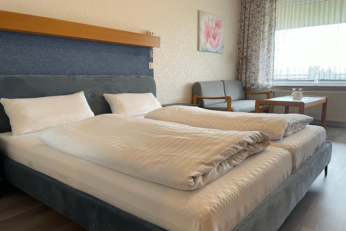 A double bed with a grey headboard, a small table with a chair, and a window with curtains.