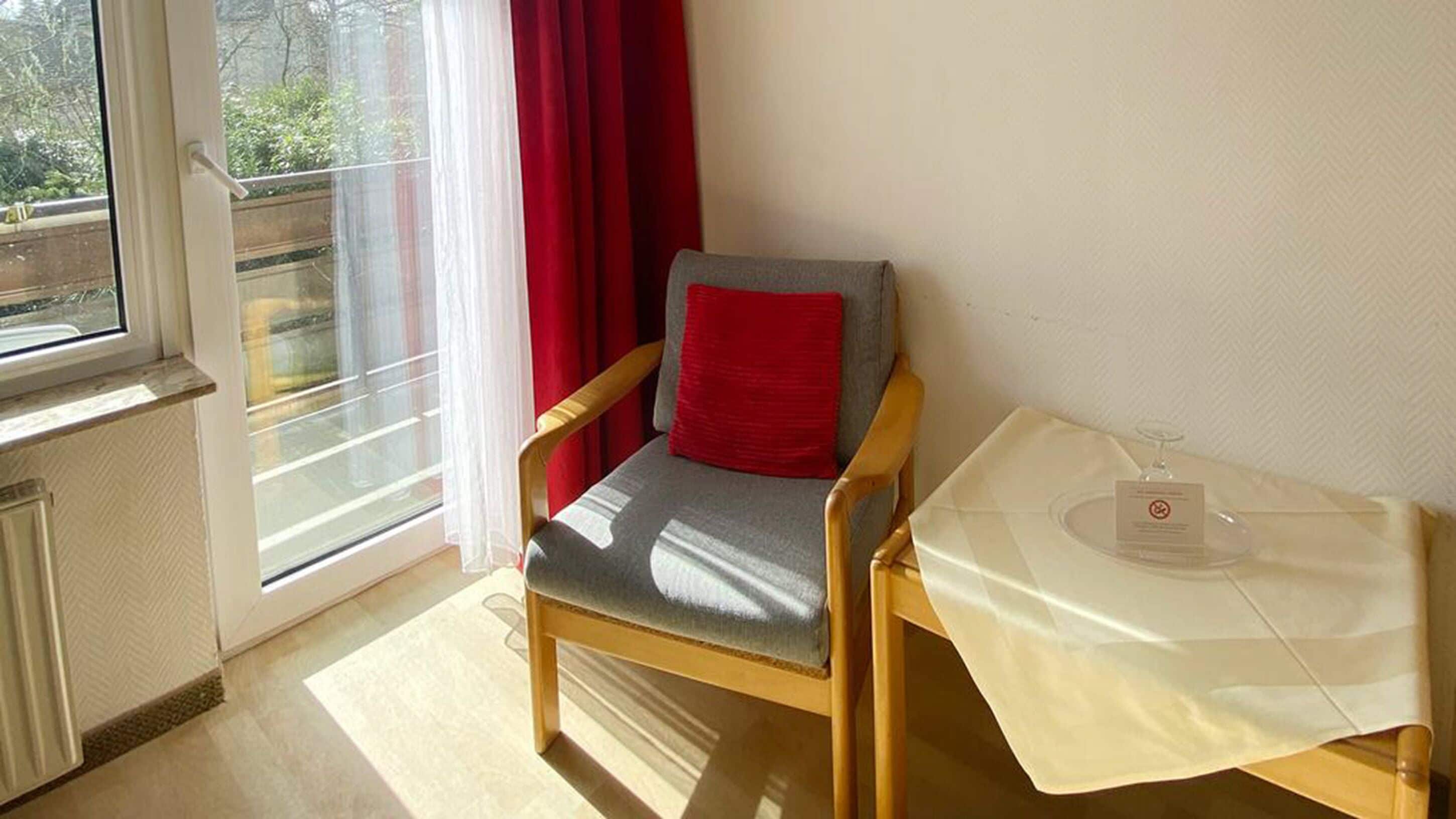 A room with a chair, a table with a glass, and a window with curtains.