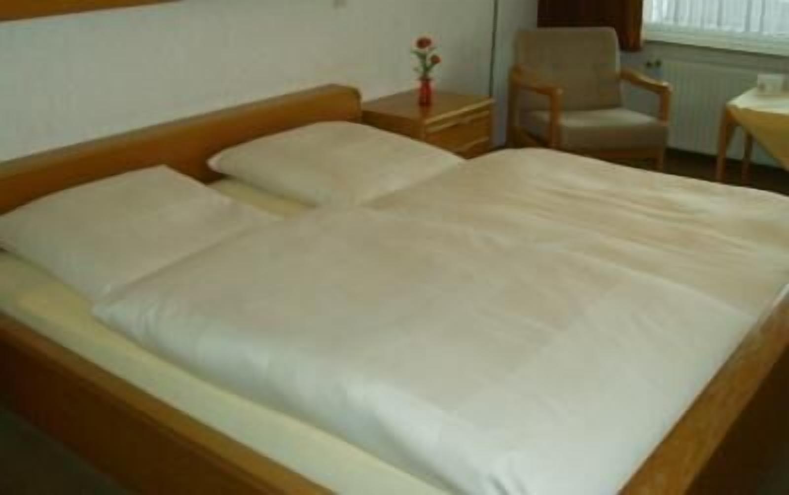 Una cama bien tendida con cabecera de madera y una mesita de noche con un florero.