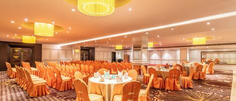 A banquet hall with round tables, orange chairs, and a carpet with a floral pattern.