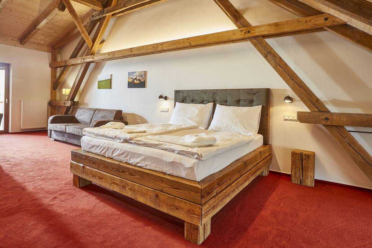 A bedroom with a wooden bed frame, a grey sofa, and a red carpet.