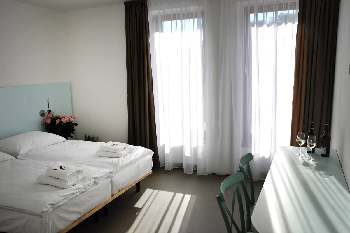 A hotel room with a bed, a table with two wine glasses and a bottle, and a chair.