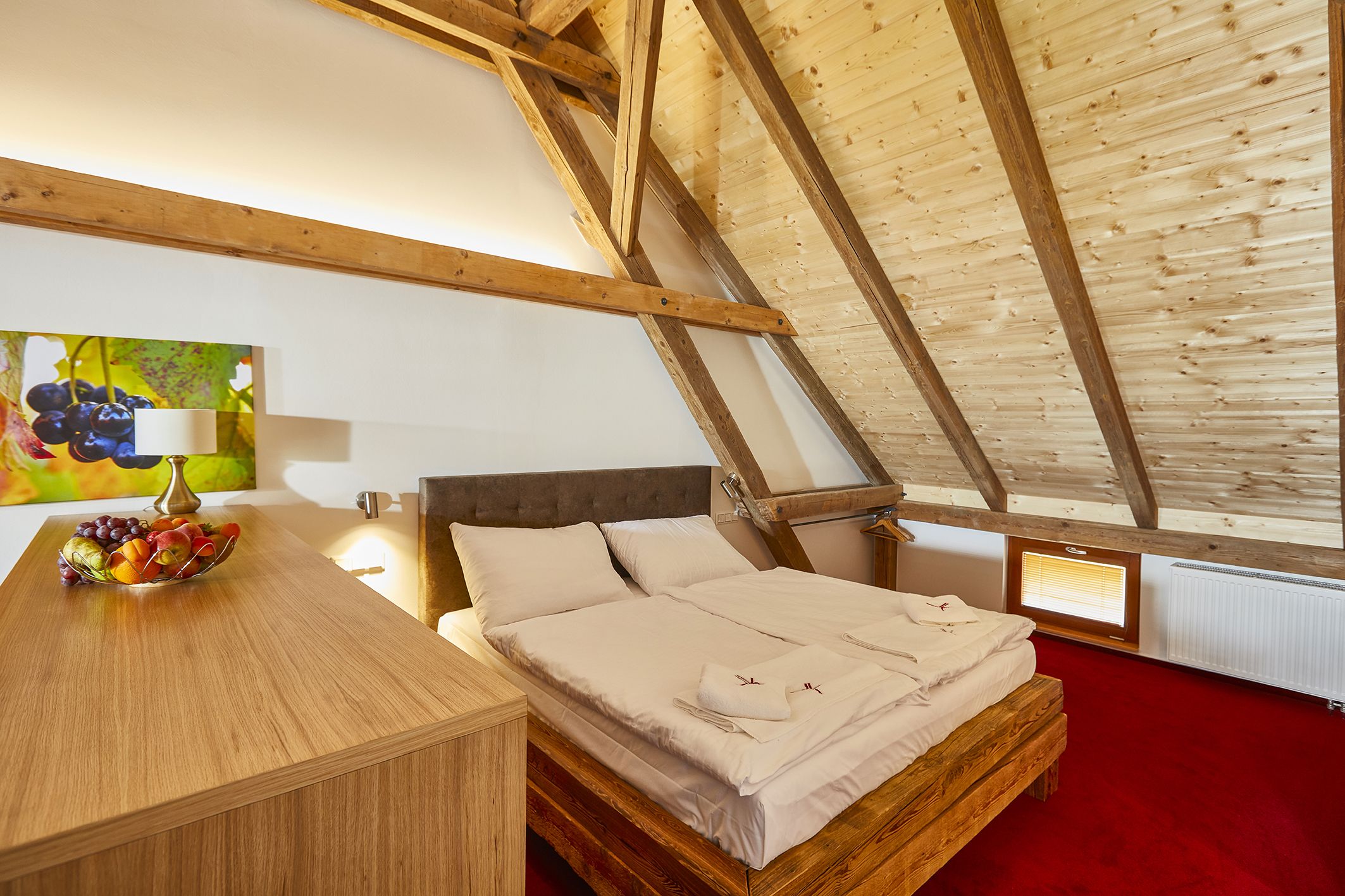Ein Schlafzimmer mit Holzboden, einem Bett mit weißen Bettwäsche, einer Obstschale auf einem Holztisch und einem Gemälde an der Wand.