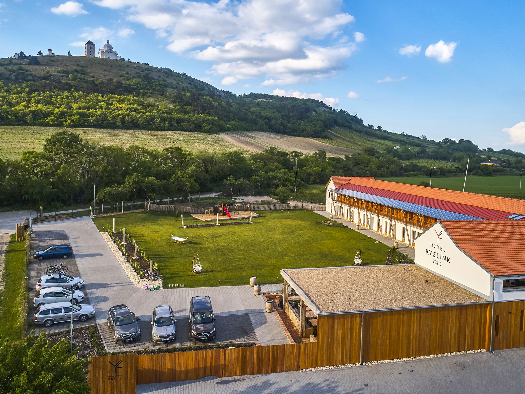 A hotel with a red roof, a parking area with several cars, and a playground.