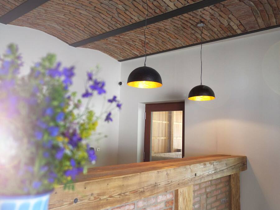 A reception area with a wooden counter and a brick wall. There are two black pendant lights with yellow shades. A potted plant with purple flowers is in the foreground.