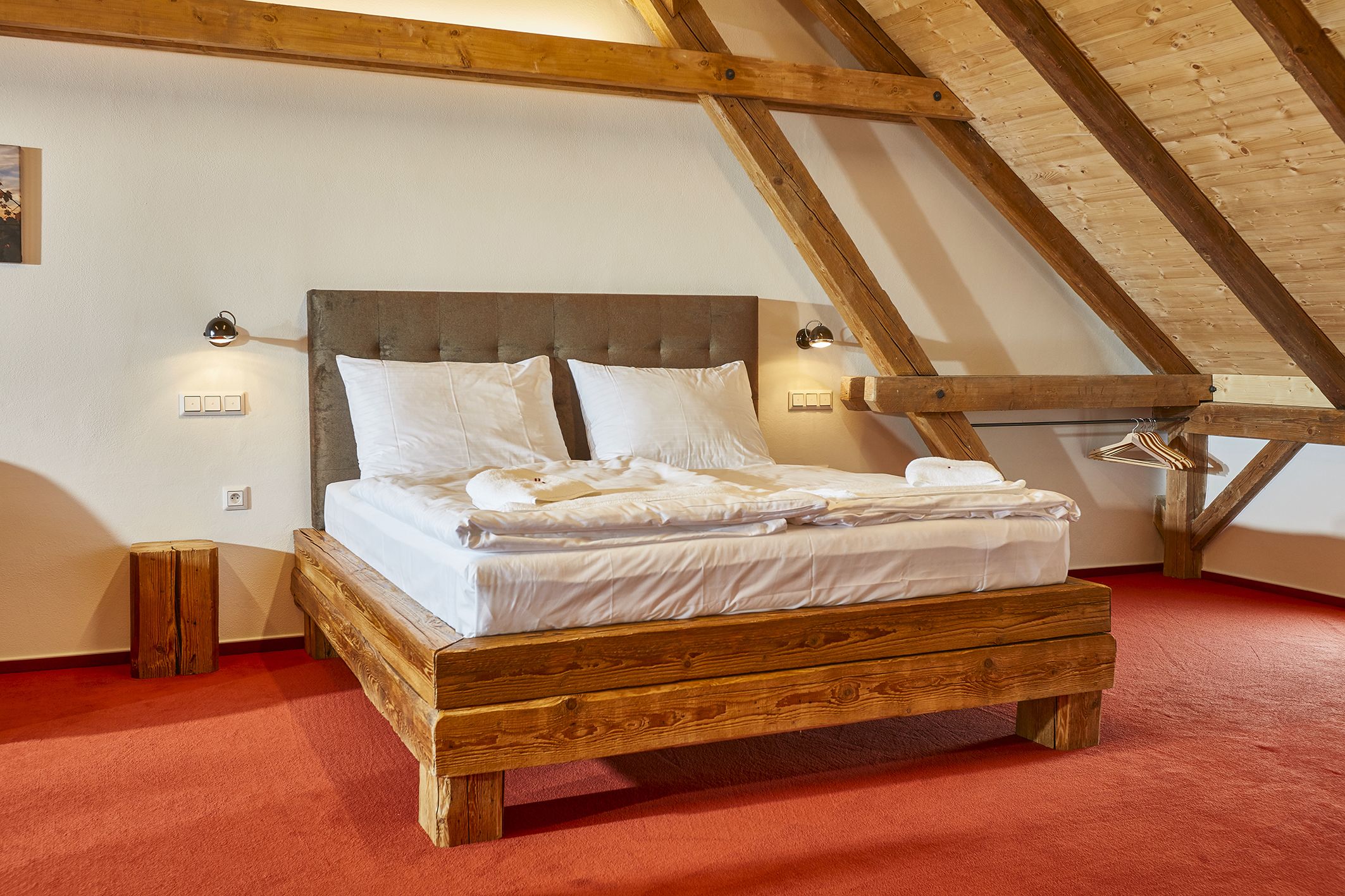 Een houten bed in een kamer met schuine plafonds en zichtbare balken.