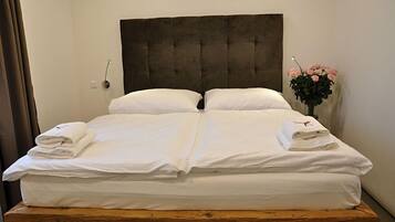 Ein Doppelbett mit weißer Bettwäsche und einem dunklen Kopfteil, ein Nachttisch aus Holz und eine Vase mit rosa Blumen.