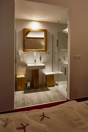 A modern bathroom with a wooden vanity, a glass shower enclosure, and a white sink.