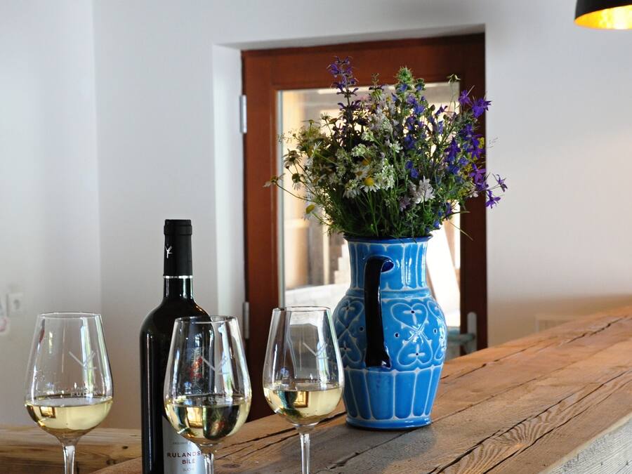A wooden table with three wine glasses, a bottle of wine, and a blue vase with flowers.