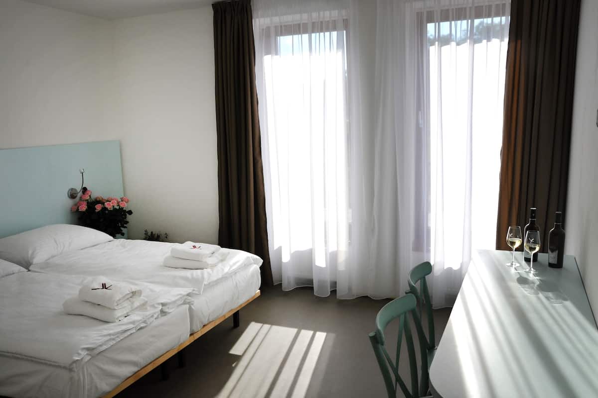 A hotel room with a bed, a table with two wine glasses and a bottle, and a chair.