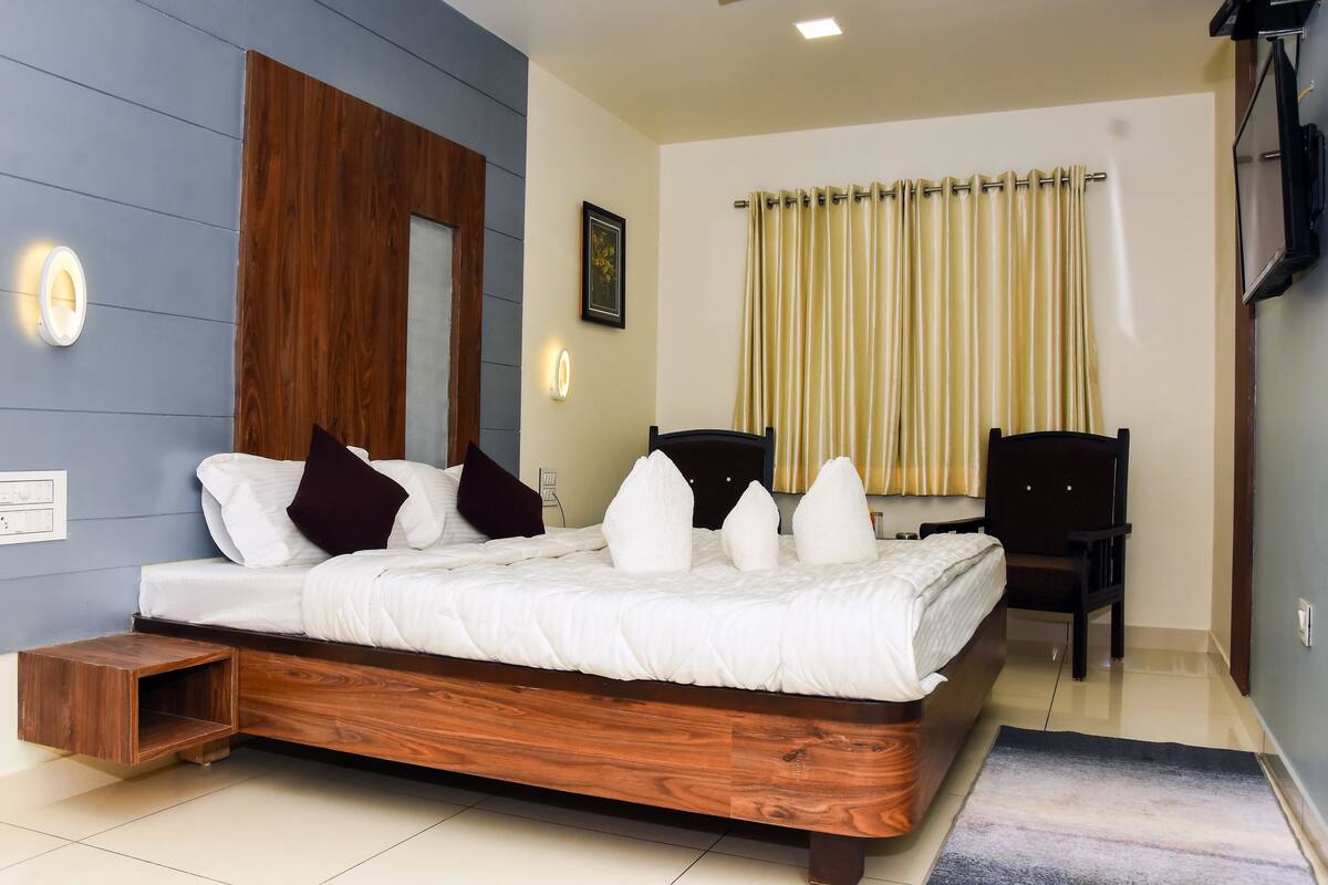 A modern bedroom with a wooden bed, a nightstand, a chair, and a large window with curtains.