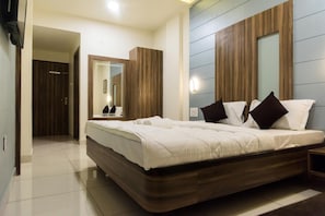 A modern bedroom with a large bed, a wooden headboard, a mirror, and a nightstand. - Hotel Shyam Palace (Bhuj)