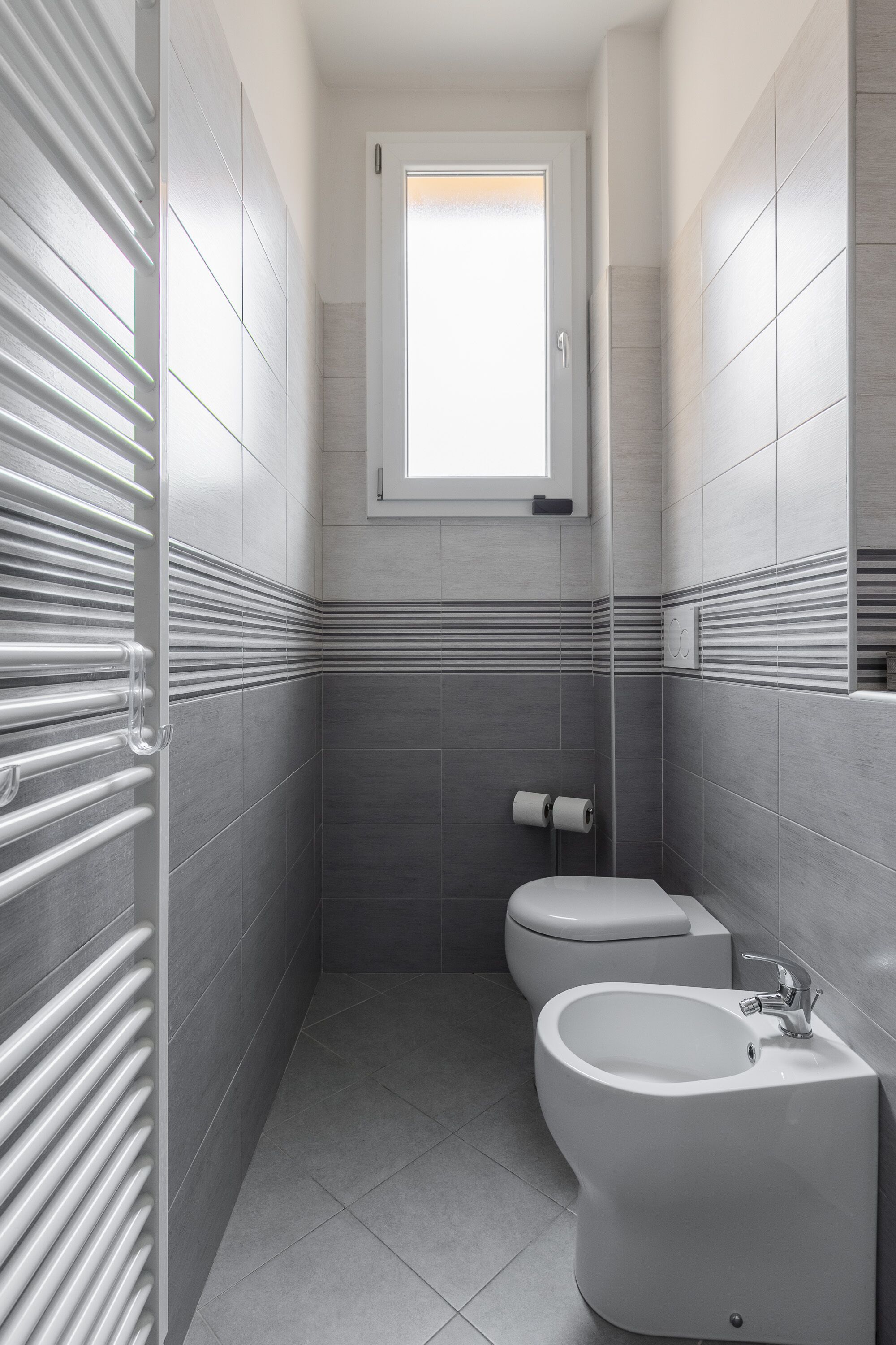 A modern bathroom with a toilet, bidet, and a window.
