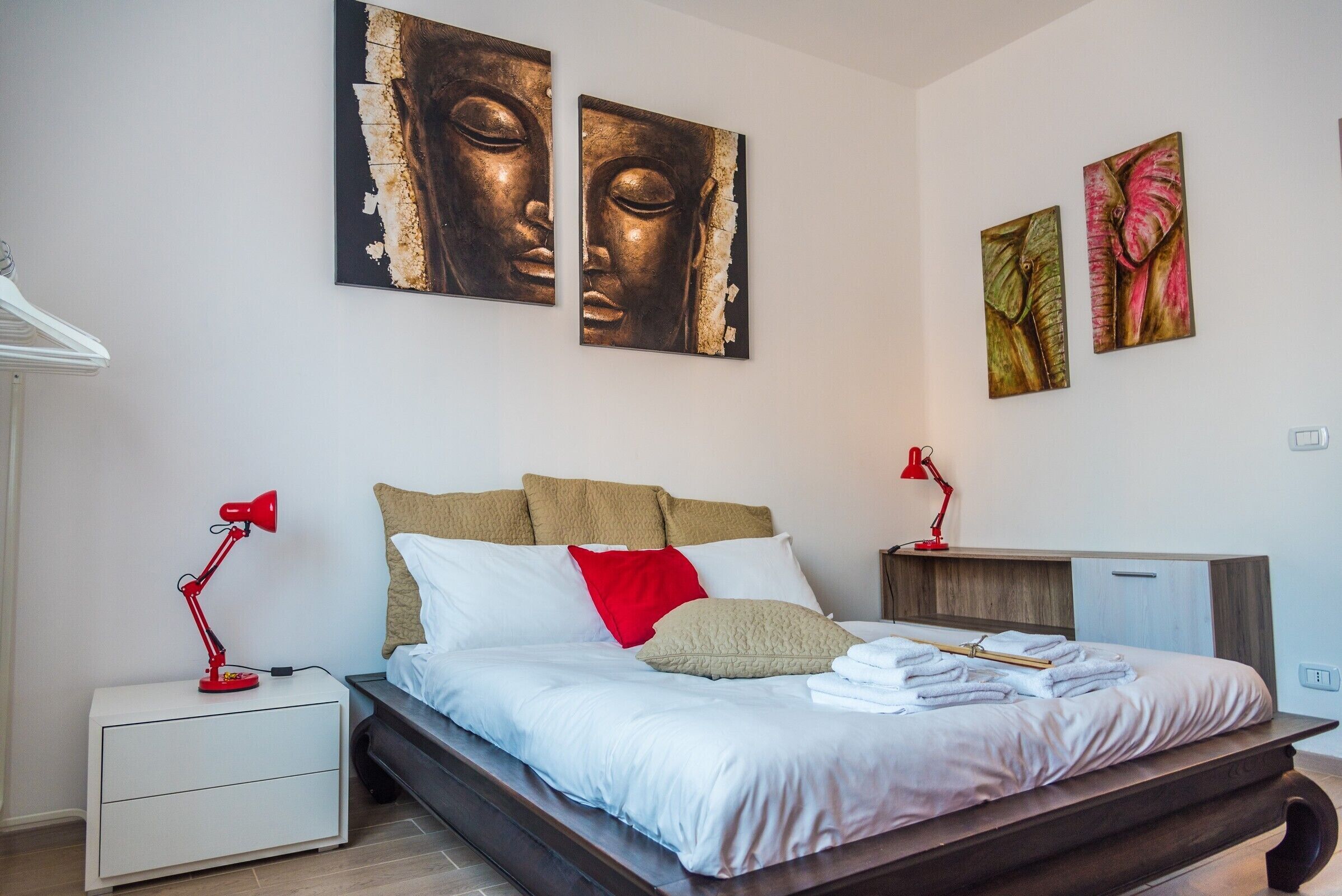 A bedroom with a bed, nightstands, a desk, and artwork on the walls.