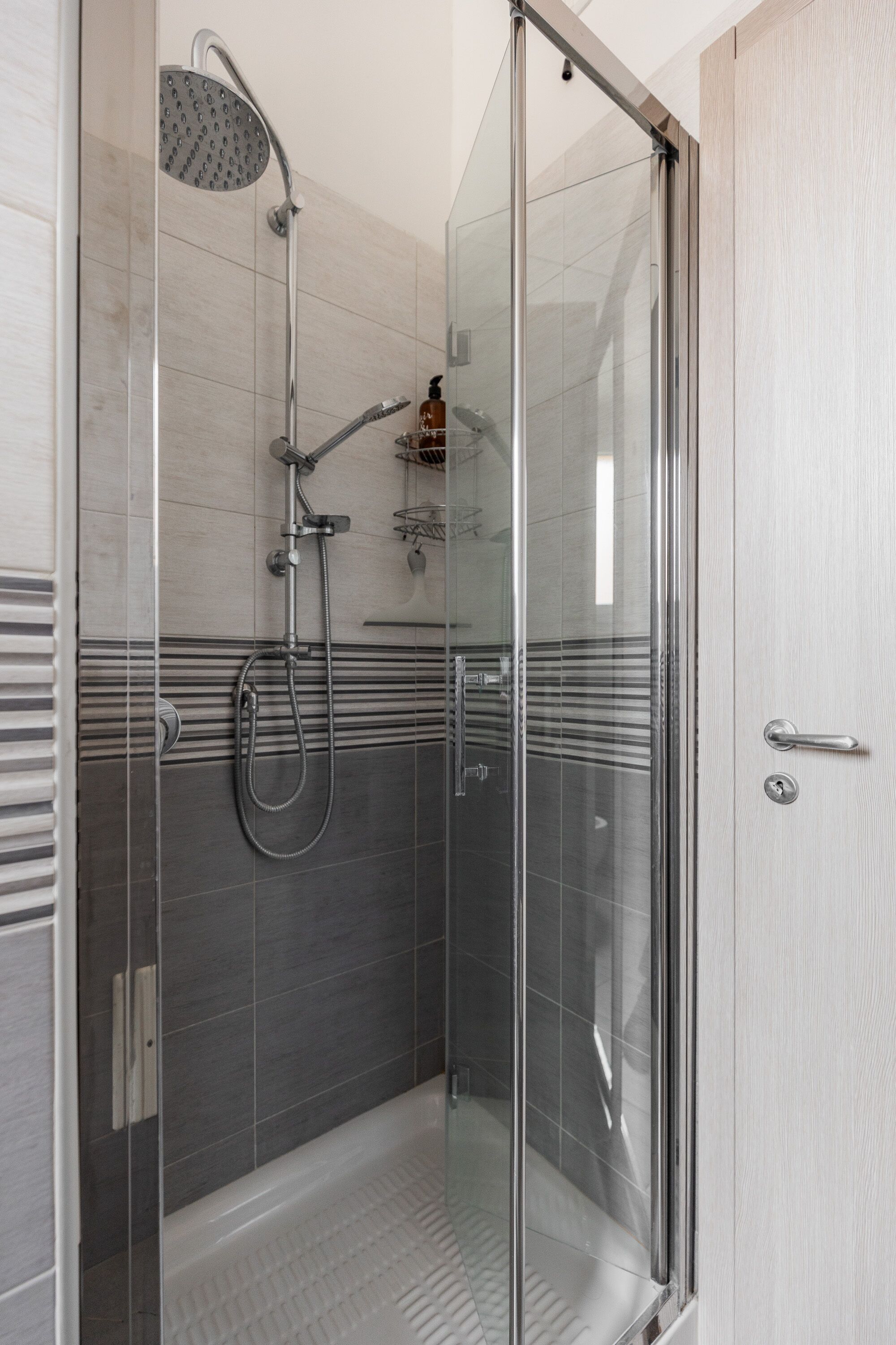 A glass-enclosed shower area with a handheld showerhead, a wall-mounted faucet, and a handheld showerhead.